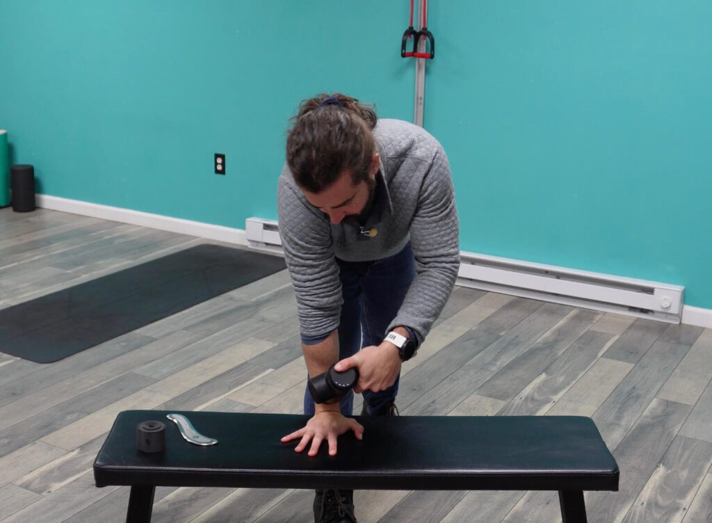 Dr. John with his wrist on a bench in extension using the massage gun through the front of the wrist